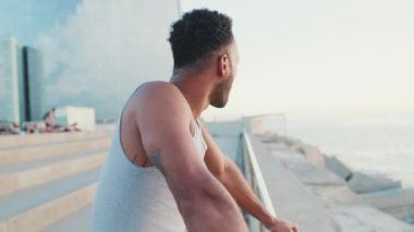 Genç, sakallı, formda bir sporcu setin üzerinde durmuş denize bakıyor. Kamera ileri gidiyor.