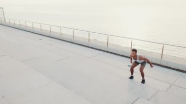 Genç sakallı erkek sporcu spor yapıyor, merdivenlerde zıplıyor.