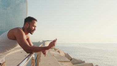 Genç sakallı erkek sporcu, sette antrenmandan sonra dinlenirken cep telefonu kullanıyor.