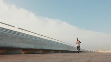 Young bearded male fit athlete runs along the promenade