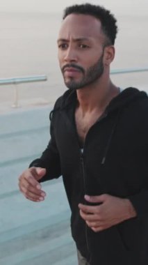 VERTICAL VIDEO: Young bearded male athlete runs along the promenade