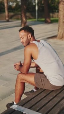 Genç sakallı erkek sporcu antrenmandan sonra bankta oturarak dinleniyor.