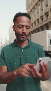 Caddenin hemen yanında duran ve telefonu kullanan genç bir adam var.