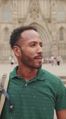 Omzunda sırt çantası olan, kameraya bakan ve eski şehrin meydanında dururken gülümseyen genç turistin yakın çekimi.