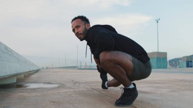 Genç sakallı erkek sporcu ısınma egzersizi yapıyor, sette antrenmandan önce bacak esnetiyor.