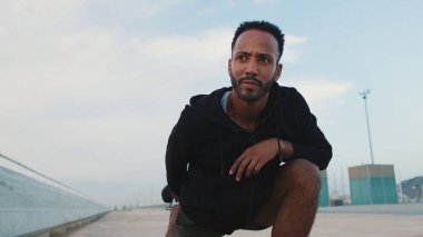 Genç sakallı erkek sporcu ısınma egzersizi yapıyor, sette antrenmandan önce bacak esnetiyor.