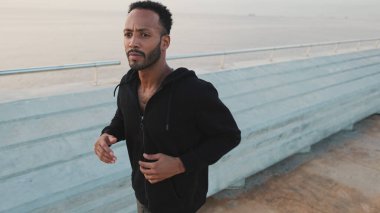 Genç sakallı erkek sporcu gezinti güvertesinde koşuyor.