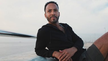 Genç sakallı erkek sporcu antrenmandan sonra sette otururken dinleniyor.