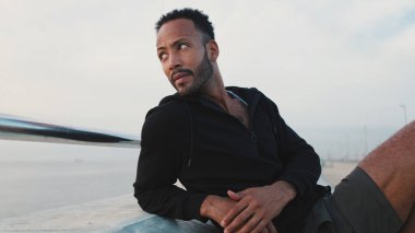 Genç sakallı erkek sporcu antrenmandan sonra sette otururken dinleniyor.