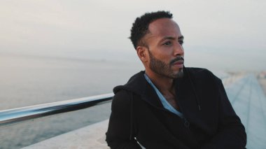 Genç sakallı erkek sporcu antrenmandan sonra sette otururken dinleniyor.