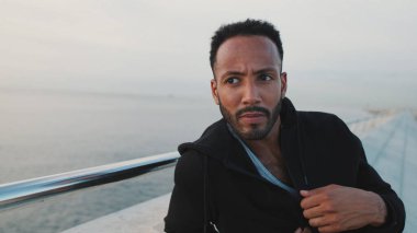 Genç sakallı erkek sporcu antrenmandan sonra sette otururken dinleniyor.