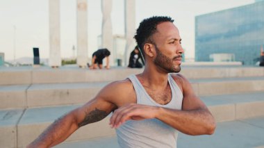 Young bearded male athlete jumps and makes movements with his hands during workout on the waterfront