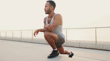 Young bearded male fit athletes stretches on the embankment