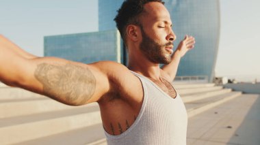 Close up, young bearded male athlete doing workout, stretching on the embankment