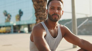 Genç sakallı erkek sporcu, eğitimden sonra modern arka planda bankta dinleniyor.