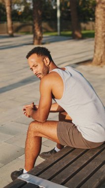 Genç sakallı erkek sporcu, eğitimden sonra modern arka planda bankta dinleniyor.