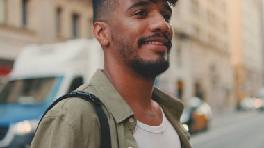 Young man with beard dressed in an olive-colored shirt crosses the road at pedestrian crossing