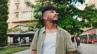 Young happy man with beard dressed in an olive-colored shirt walks along the street of the old city, looks to the side