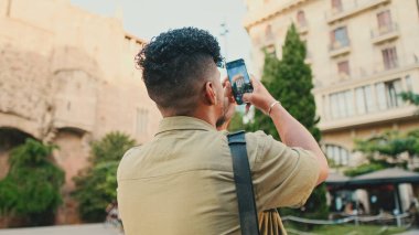 Close up, young man dressed in an olive-colored shirt takes photo on the street of the old city