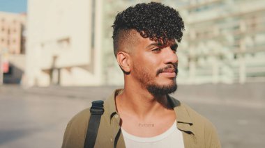 Close up, young smiling man dressed in an olive-colored shirt walks along the narrow street of the old city and looks around