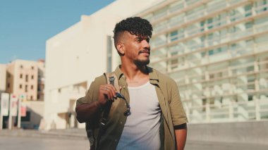 Close up, young smiling man dressed in an olive-colored shirt walks along the narrow street of the old city and looks around