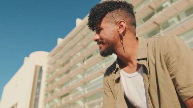 Young male student dressed in an olive colored shirt sits outside next to university