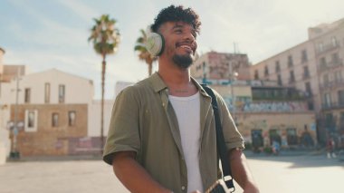 Young man with beard in an olive-colored shirt listens to music on headphones, dances