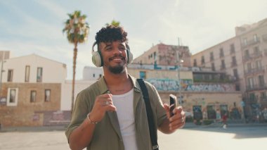 Young man with beard in an olive-colored shirt listens to music on headphones, dances