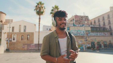 Young man with beard in an olive-colored shirt listens to music on headphones, dances