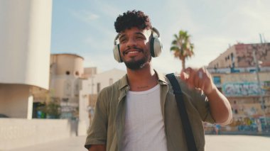Young man with beard in an olive-colored shirt listens to music on headphones, dances