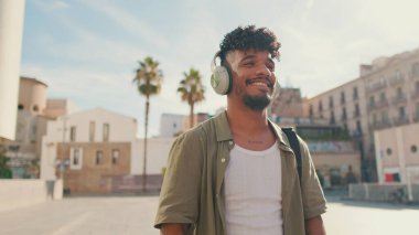 Young man with beard in an olive-colored shirt listens to music on headphones, dances