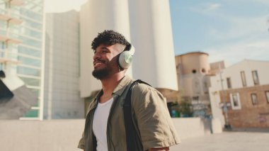 Young man with beard in an olive-colored shirt listens to music on headphones, dances