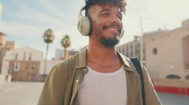 Young man with beard in an olive-colored shirt listens to music on headphones, dances