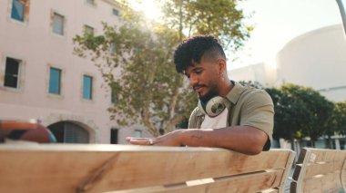 Close up, young man with beard wearing an olive colored shirt with headphones sends voice message