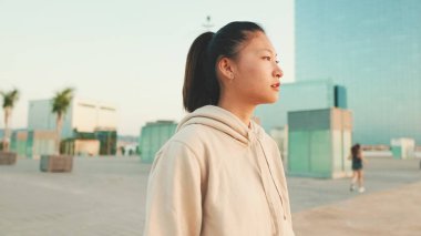 Close up, asian girl in sportswear stands at morning time on modern buildings background