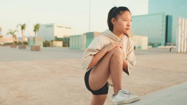 Asian girl in sportswear does workout, stretching and gymnastics on modern buildings background
