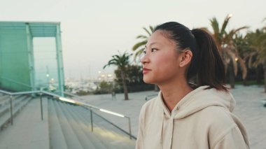 Asian girl wears sportswear, climbs stairs, looks up at morning time