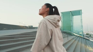 Asian girl wears sportswear, climbs stairs, looks up at morning time
