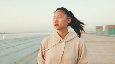 Close up, asian girl in sportswear stands at morning time on modern buildings background