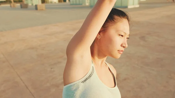 Asian girl in sports top does workout, stretching and gymnastics at morning time.