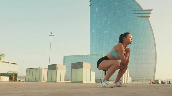 Asian girl in sports top does workout, squats, quadriceps exercises at morning time