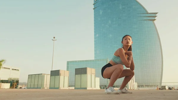 Asian girl in sports top does workout, squats, quadriceps exercises at morning time