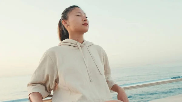 Asian girl wears sportswear sits on the promenade at morning time, on the background of the sea