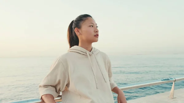 Asian girl wears sportswear sits on the promenade at morning time, on the background of the sea