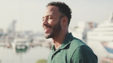 Genç gülen adam limanda arka planda yatlarla oturuyor.