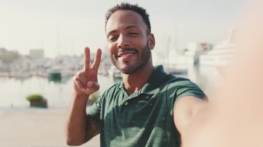 Limanda arka planda yatlarla otururken telefondan video görüşmesi yapan mutlu genç adam.