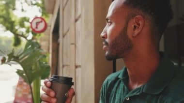 Yakın plan, genç adam şehir manzarası arka planında sokak kafesinde otururken kahve içiyor.