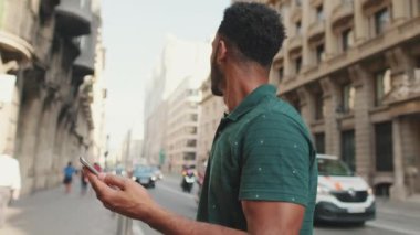 Genç adam telefonunda harita uygulaması kullanıyor, etrafa bakıyor.