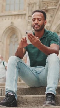 Genç adam Barcelona 'daki Sagrada Familia' nın merdivenlerinde otururken cep telefonu kullanıyor.