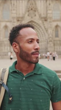 Omzunda sırt çantası olan, kameraya bakan ve eski şehrin meydanında dururken gülümseyen genç turistin yakın çekimi.